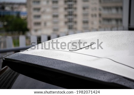 Close-up white GPS antenna shark fin shape on a roof of car for radio navigation system. Antenna shark fin on blurry background with raindrops. Car detail