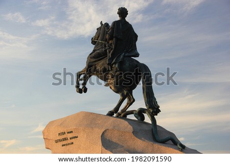 Back view of the Bronze Horseman statue of Peter the Great situated in the Senate Square in St. Petersburg in Russia, the statue in illuminated by golden sunlight, blue cloudy sky is in the background Royalty-Free Stock Photo #1982091590