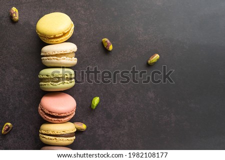 Row of colorful macarons and pistachios isolated. French meringue cookie macaron. Top view. Dark background. Banner copy space.