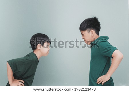 Two angry siblings looking each other on grey background Royalty-Free Stock Photo #1982121473