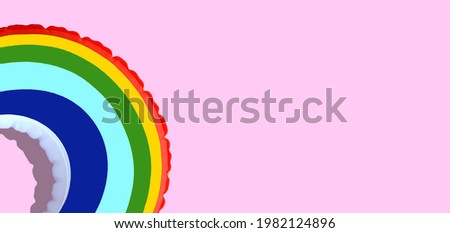 Rainbow inflatable swimming pool ring on pink background.