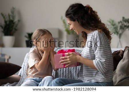 Loving young Hispanic mother congratulate excited small daughter with birthday give wrapped gift. Caring happy Latin mom greeting make surprise with present for little girl child, celebrate together.