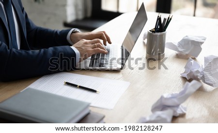 Businessman using laptop among crumpled paper drafts messy in office. Professional typing important document on keyboard, writing article or report, working at computer. Close up of hands Royalty-Free Stock Photo #1982128247