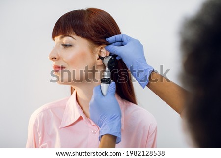 Hearing loss and otitis treatment concept. Close up of female young patient having check up at ENT doctor. Unrecognizable otorhinolaryngologist looking at patients ear with otoscope