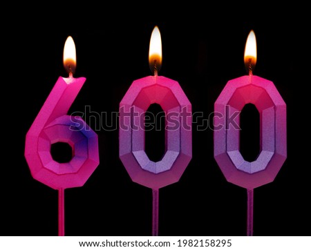 Pink and blue burning birthday candles isolated on black background, number 600