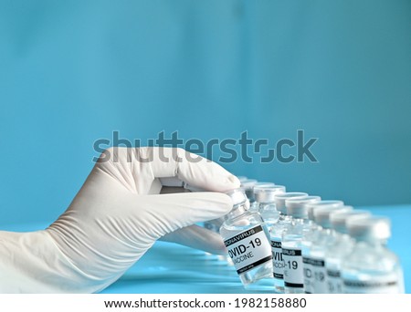 Doctor or nurse holding Coronavirus COVID-19 Vaccine Glass Bottle on blue surface with blue background at Thailand. Concept viruses spread throughout the world. Selective Focus.