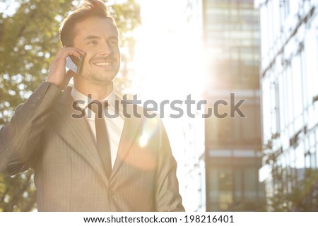 Happy young businessman using cell phone outdoors