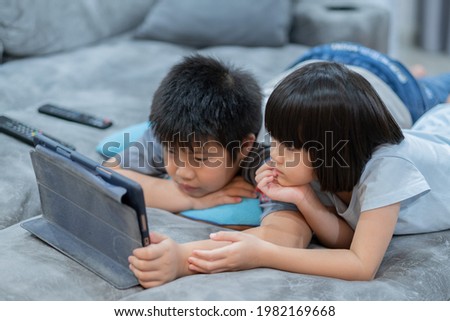 two children addicted tablet, asian kid watching cartoon
