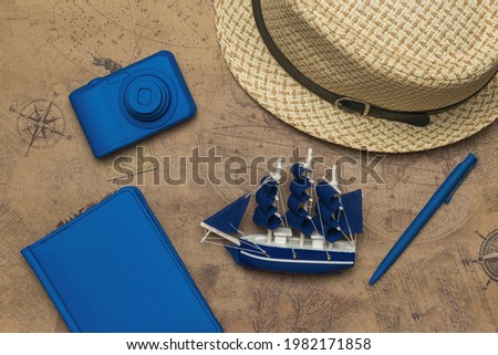 A hat, a camera, a notebook and a model of a sailboat on the background of an old map. The concept of travel planning.