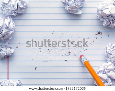 School supplies of blank lined notebook paper with eraser marks and erased pencil writing, surrounded by balled up paper and a pencil eraser. Studying or writing mistakes concept. Royalty-Free Stock Photo #1982172035