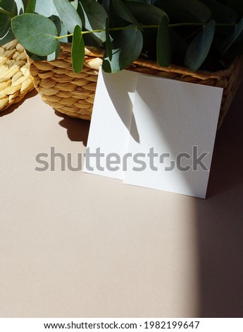 Card mockup with copy space from straw box and eucalyptus leaves with sunlight shadow. Greetings, wedding invitations blank, paper sheet on beige background.  Summer stationary template.