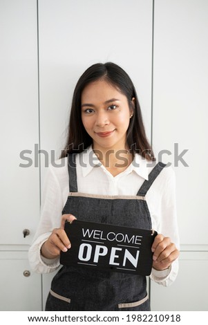 Portrait of waitress in apron holding open sign board while standing in coffee shop.