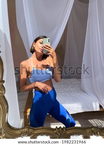 Fit tanned woman in sportswear, perfect body, abs motivation, at home take photo selfie on phone in mirror for social media, stories, vertical