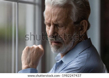 Close up sad older 70s man standing near window with eyes closed. Lonely vulnerable abandoned bearded grandfather suffer about disorder, incurable senile disease, widower portrait, loneliness concept Royalty-Free Stock Photo #1982247437