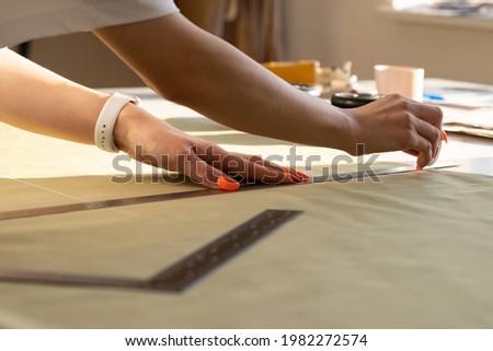 Creating clothes concept: unrecognizable female seamstress work with draft and fabric on sewing table. Garment factory or atelier small business owner create new collection of trendy apparel in studio