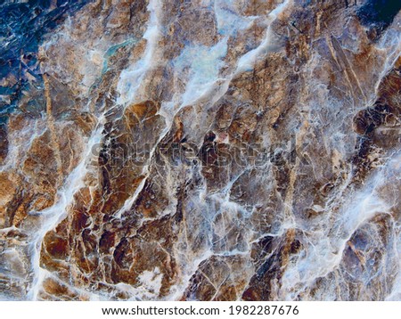 Marble cracks vein background texture of mountain cliff.Textured grunge photo of natural rock formation structure wall layers stone wallpaper pattern design.Marbled grey blue brown yellow white colors