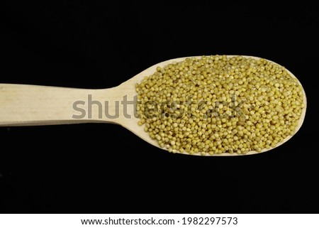 Millet in wooden spoon on black background