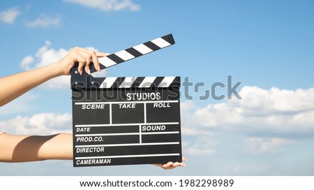 Asian woman holding clapper board with blue sky grass field, open landscape view. Hands holding film slate cinema clapper on spring background. Film making video shooting production outdoors footage