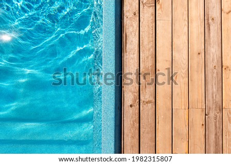 New modern fiberglass plastic swimming pool entrance step with clean fresh refreshing blue water on bright hot summer day at yard or resort hotel spa area. Wooden flooring deck of teak or larch board Royalty-Free Stock Photo #1982315807