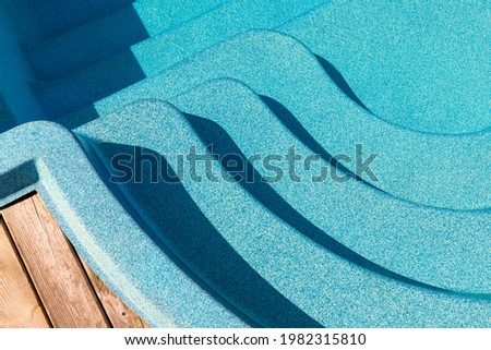 New modern fiberglass plastic swimming pool entrance step with clean fresh refreshing blue water on bright hot summer day at yard or resort hotel spa area. Wooden flooring deck of teak or larch board Royalty-Free Stock Photo #1982315810