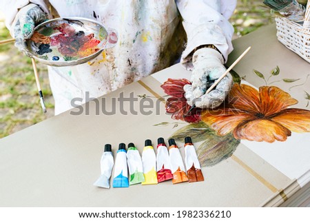 unrecognizable person painting flowers with a brush on an old wooden furniture. Artist using his color palette with various acrylic paints on a wooden table.