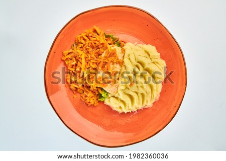 Mashed potatoes with carrots, herbs and red fish in an orange round plate on a white background.