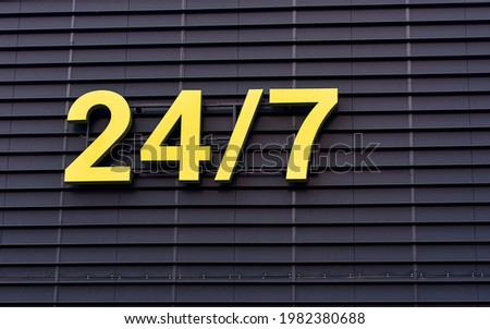 24 hours yellow sign open or working around the clock hanging on dark wall. Shop working 24 hours, sign on facade of building. 