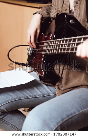 crop view of a young woman playing elecrtic guitar. bass guitarist reading chords notes and play in studio. Royalty-Free Stock Photo #1982387147