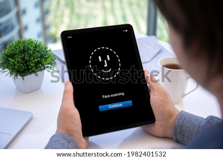 male hands holding computer tablet with face scanning application on screen over table in cafe 