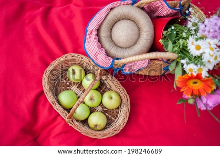 Healthy picnic for a summer vacation with fresh apples flowers, laid out on a red checked cloth with wicker basket