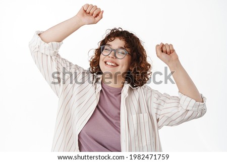 Dancing natural girl having fun, rasing hands up and partying, smiling carefree with closed eyes, relaxing in casual clothes, standing over white background Royalty-Free Stock Photo #1982471759