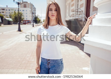 Attractive girl in white blank t-shirt stands on the street.