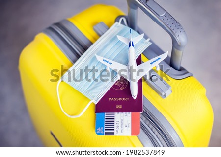 Traveling during covid-19 pandemic. Yellow luggage, medical mask, passport with ticket and toy plane.
