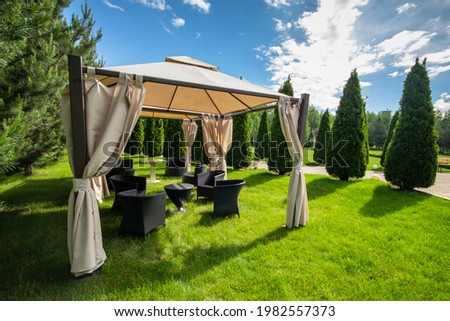 White canvas gazebo with plastic garden furniture in a summer green lawn. Royalty-Free Stock Photo #1982557373