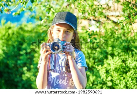 Cute little girl in cap takes picture with camera for mom in nature, outdoor .Vacation Travel lifestyle, Education and Smart kid girl concept. 