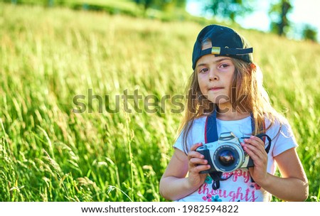 Cute little girl in cap takes picture with slr camera in nature, outdoor .Vacation Travel lifestyle, Education and Smart kid girl concept. 