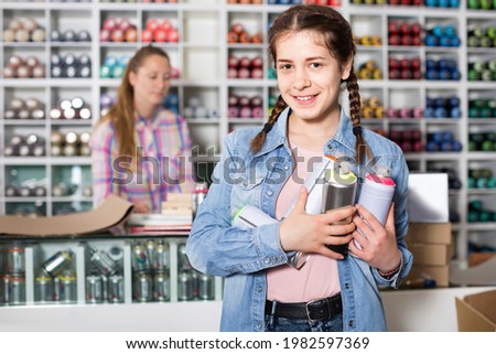 Portrait of happy cheerful positive girl choosing paint color in aerosol can in art shop Royalty-Free Stock Photo #1982597369