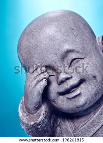 Close Up Laughing Stone Buddah Isolated On Blue Background A young buddah made out of stone, happy expression, laughing about himself.