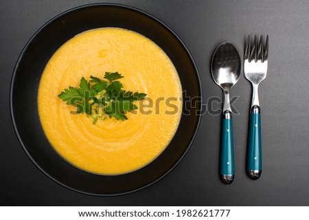 carrot puree soup in a black bowl on a black background. View from above