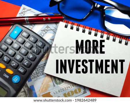 Business concept.Notebook with text MORE INVESTMENT with calculator,pen,,banknote and glasses on blue and red background
