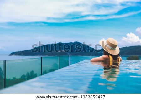 Summer travel vacation concept, Happy traveler asian woman with hat and bikini relax in luxury infinity pool hotel resort at day in Phuket, Thailand