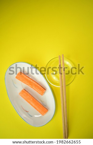 brown wooden wood chopstick with orange 
Crab sticks on cute white ceramic plate bright yellow beautiful abstract background