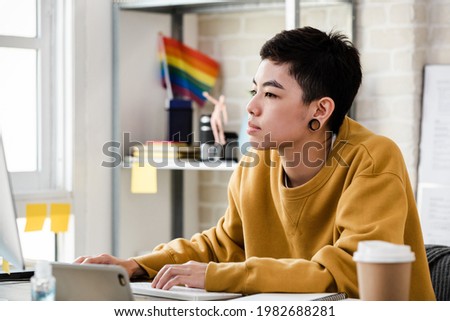 Young Asian tomboy woman in casual attire working from home in living room Royalty-Free Stock Photo #1982688281