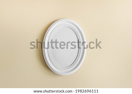 Round oval white frame with white blank oval frame on yellow textured wall.