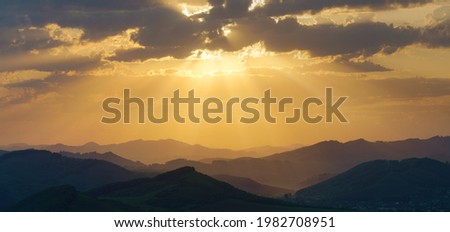 Picturesque sunrise in the mountains, sun rays through the clouds