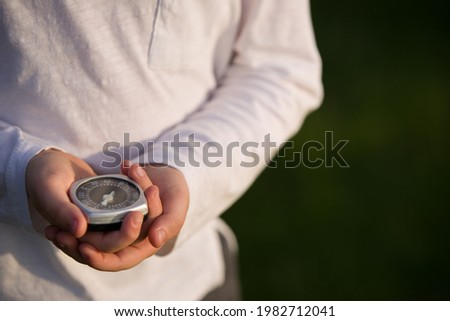 A boy in a white shirt with a compass in his hands chooses the direction of movement in the forest