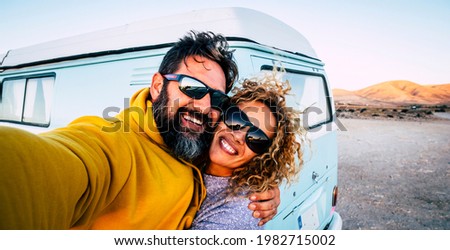 Happy adult couple smile and have fun together taking selfie picture with old vintage classic van in background - concept of vanlife and travel people - changing life man and woman