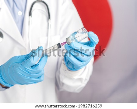 The hand of a doctor holding a vaccine bottle and syringe prepares vaccination against the background of the Japanese flag. Vaccine for immunization and treatment from virus infection.