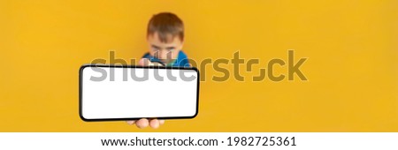 The child holds the phone in his hand for advertising on a yellow background. Color