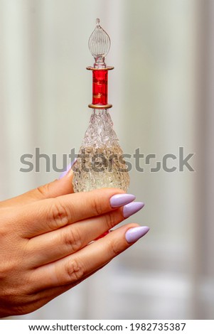 A woman's hand holds a bottle of perfume on a light background. A perfume for women, a subtle and expensive fragrance.